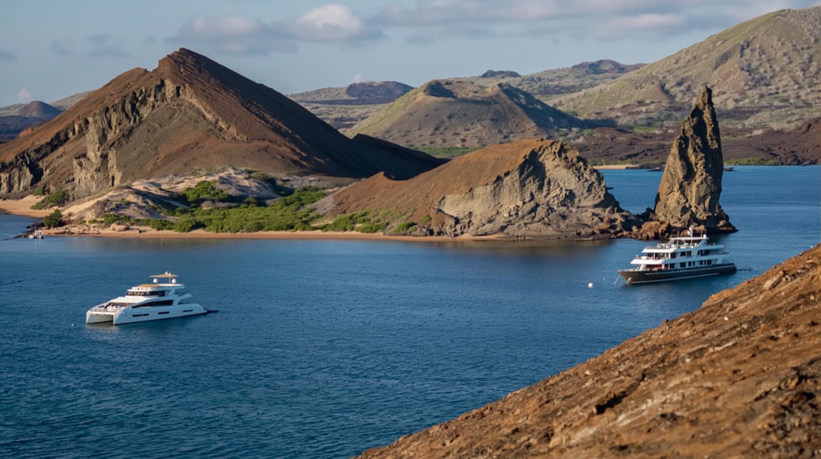 Three Galapagos expedition vessels of different size classes anchored together off a volcanic shoreline.